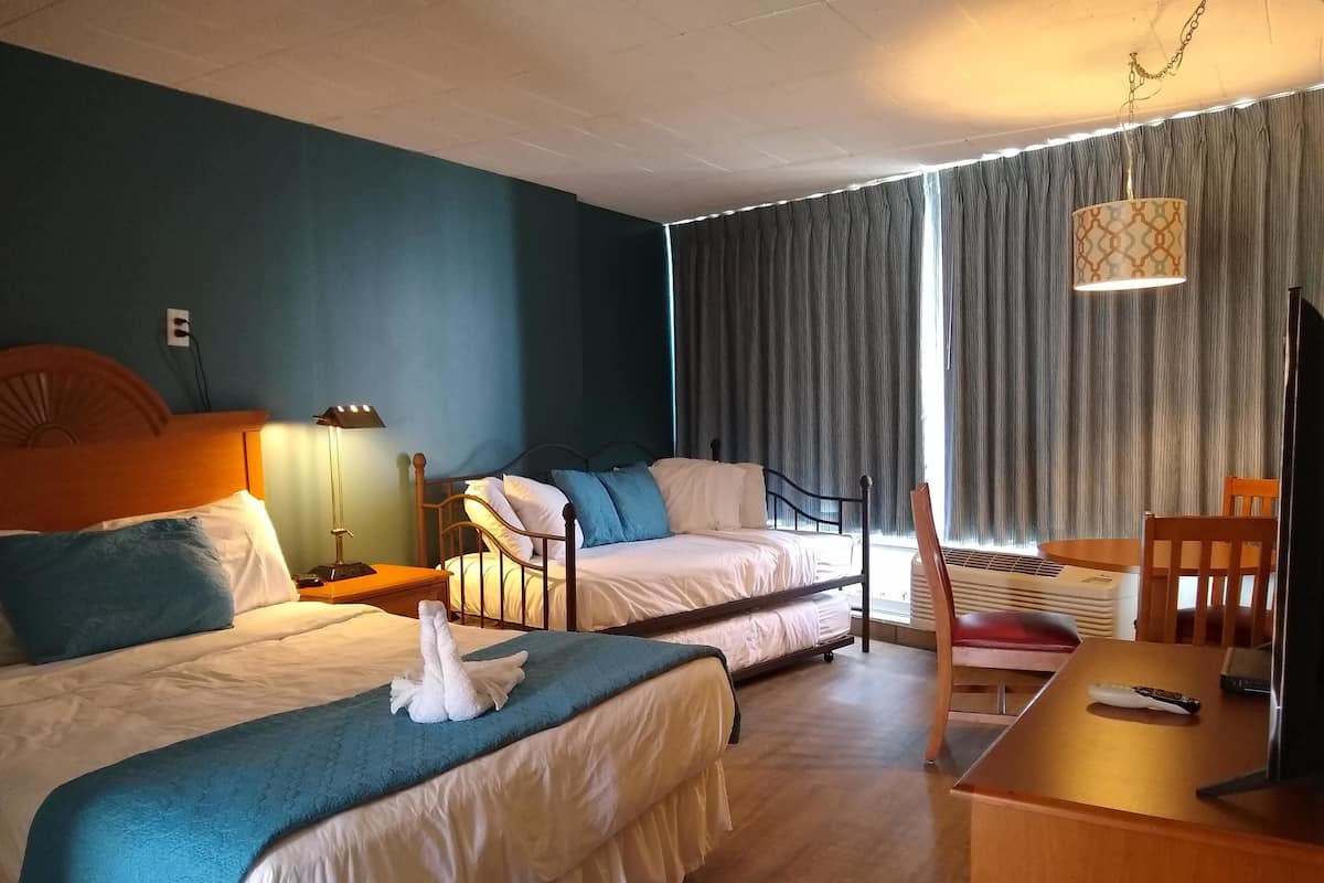 A hotel room with two beds, a desk, a chair, a TV, and a window with curtains.