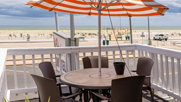 A covered outdoor seating area with a table and chairs, overlooking a beach. - Charlroy Motel (Seaside Park)