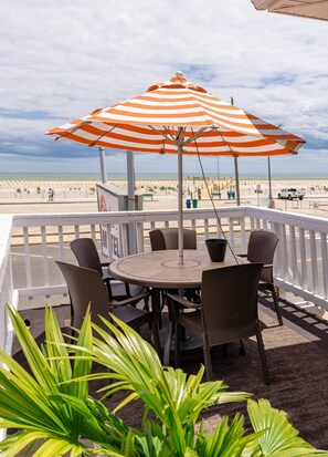 A covered outdoor seating area with a table and chairs, overlooking a beach. - Charlroy Motel (Seaside Park)