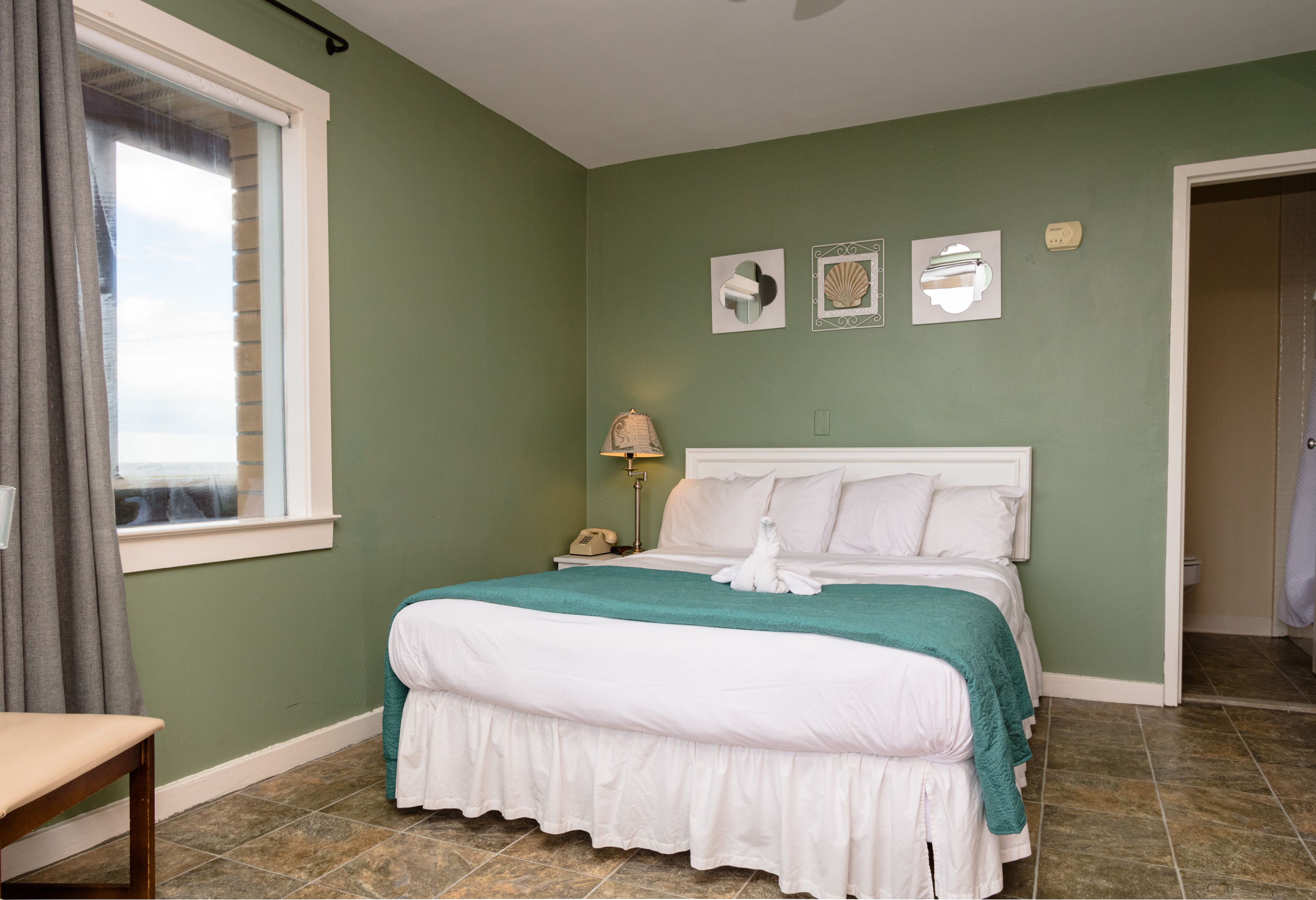 A neatly made bed with a white and teal bedspread, a bedside lamp, and a nightstand with a phone.