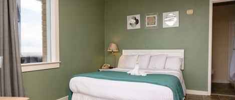 A neatly made bed with a white and teal bedspread, a bedside lamp, and a nightstand with a phone.