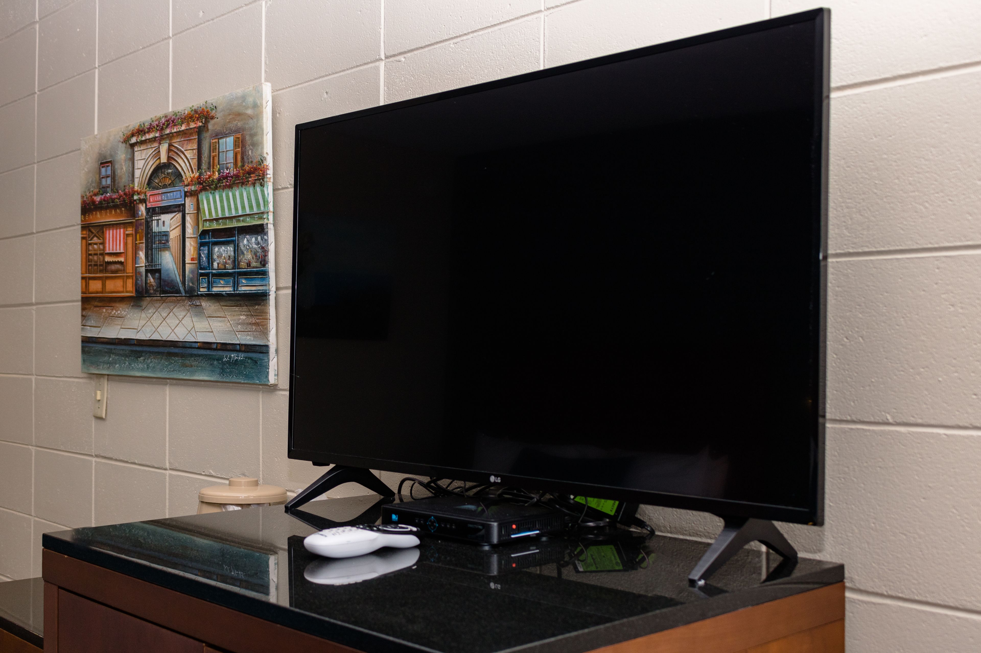 A flat-screen TV on a black stand, a remote control, and a streaming device on a counter.