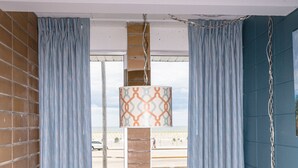 A round table with four wicker chairs, a hanging light fixture, and a view of the street through a window with blue curtains. - Charlroy Motel (Seaside Park)