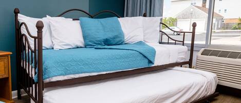 A bed with a wooden frame, white bedding, and a blue quilt.