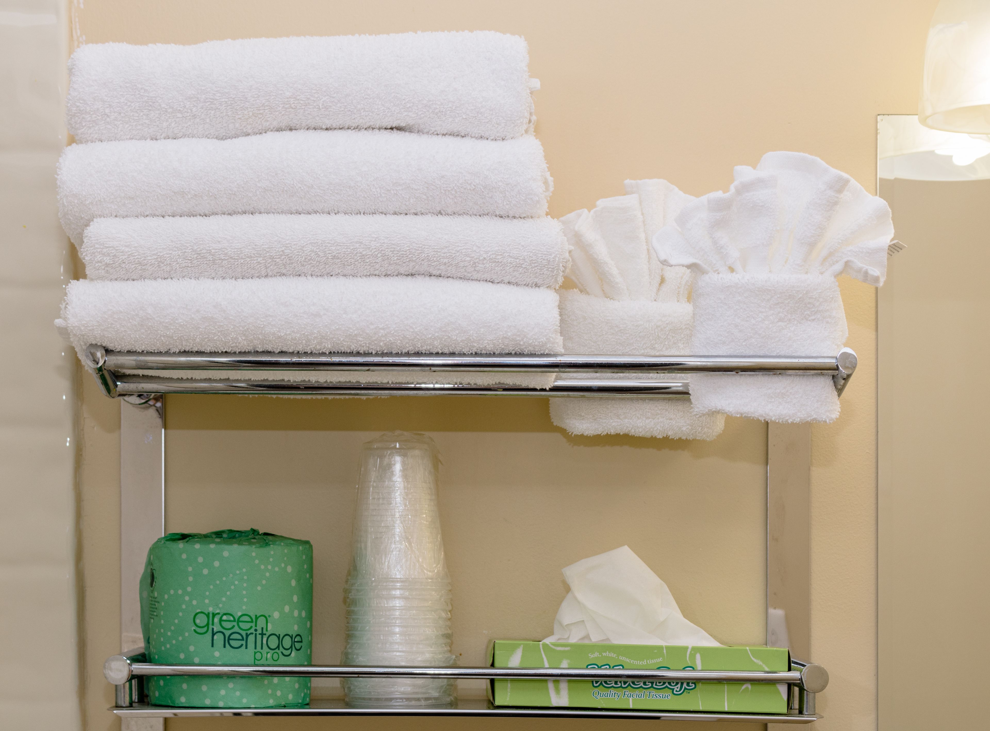 A bathroom shelf with white towels, a green tissue box, and a stack of paper towels.