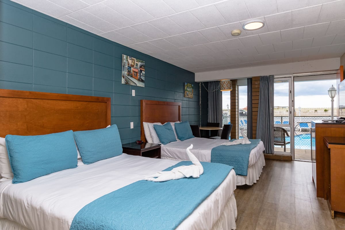 A hotel room with two beds, a dining area, and a view of the pool.