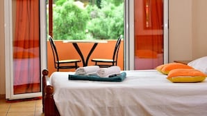 A hotel room with a bed, a table with towels, and a view of greenery through the window. - Arianna Studios And Apartments (Corfu)