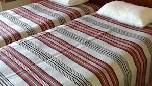 Een hotelkamer met twee bedden, gestreept beddengoed, een houten hoofdeinde, een schilderij aan de muur en twee wandlampen.