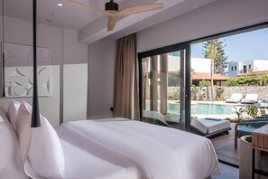 A modern hotel room with a large bed, a ceiling fan, a view of a swimming pool, and a balcony with outdoor seating. - Noble Hotel Suites (Hersonissos)