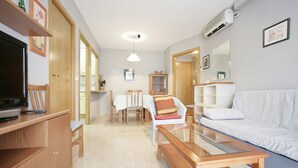 A modern living room with a flat-screen TV, wooden furniture, a glass coffee table, and a white sofa. - Larimar Apt (Salou)