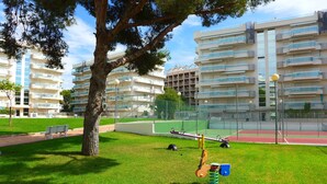 A park with a playground, a bench, and a tennis court. - Larimar Apt (Salou)