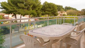 A balcony with a table and chairs, overlooking a road and trees. - Larimar Apt (Salou)