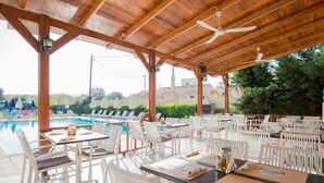 Ein Außenbereich mit Essbereich, weißen Stühlen und Tischen, einem Pool und einem überdachten Bereich mit Deckenventilator.