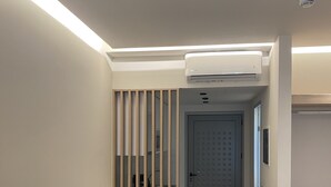 Ein modernes, minimalistisches Zimmer mit einem weißen Tisch, zwei schwarzen Stühlen, einer Trennwand aus Holzleisten, einer Tür mit Zahlenschloss und einer Klimaanlage.