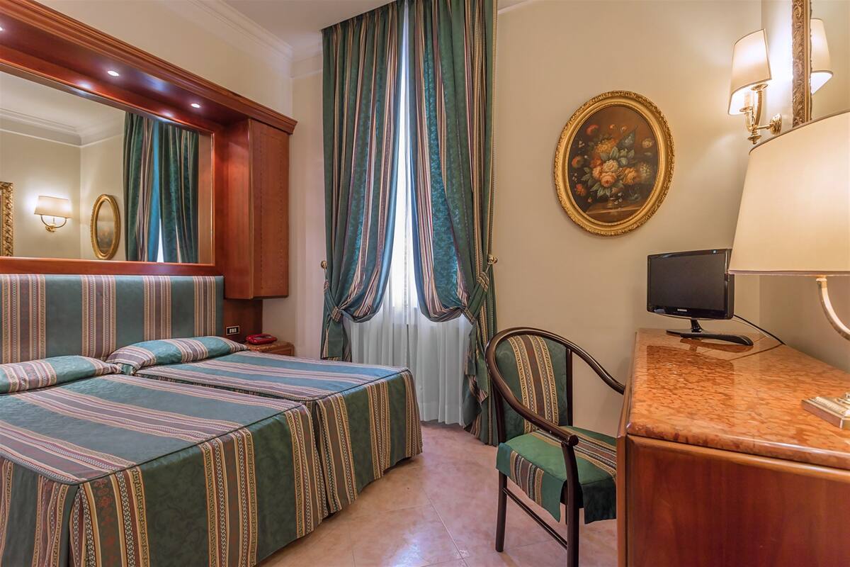 Une chambre d’hôtel avec deux lits, un bureau avec une télévision, une chaise et un grand miroir.