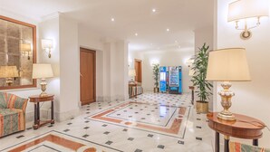 A hotel lobby with a marble floor, a sofa, a lamp, and a reception desk. - Raeli Hotel Luce (Rome)