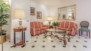 A living room with two striped sofas, a coffee table, a side table with a lamp, a chair, and a large mirror on the wall. - Raeli Hotel Luce (Rome)