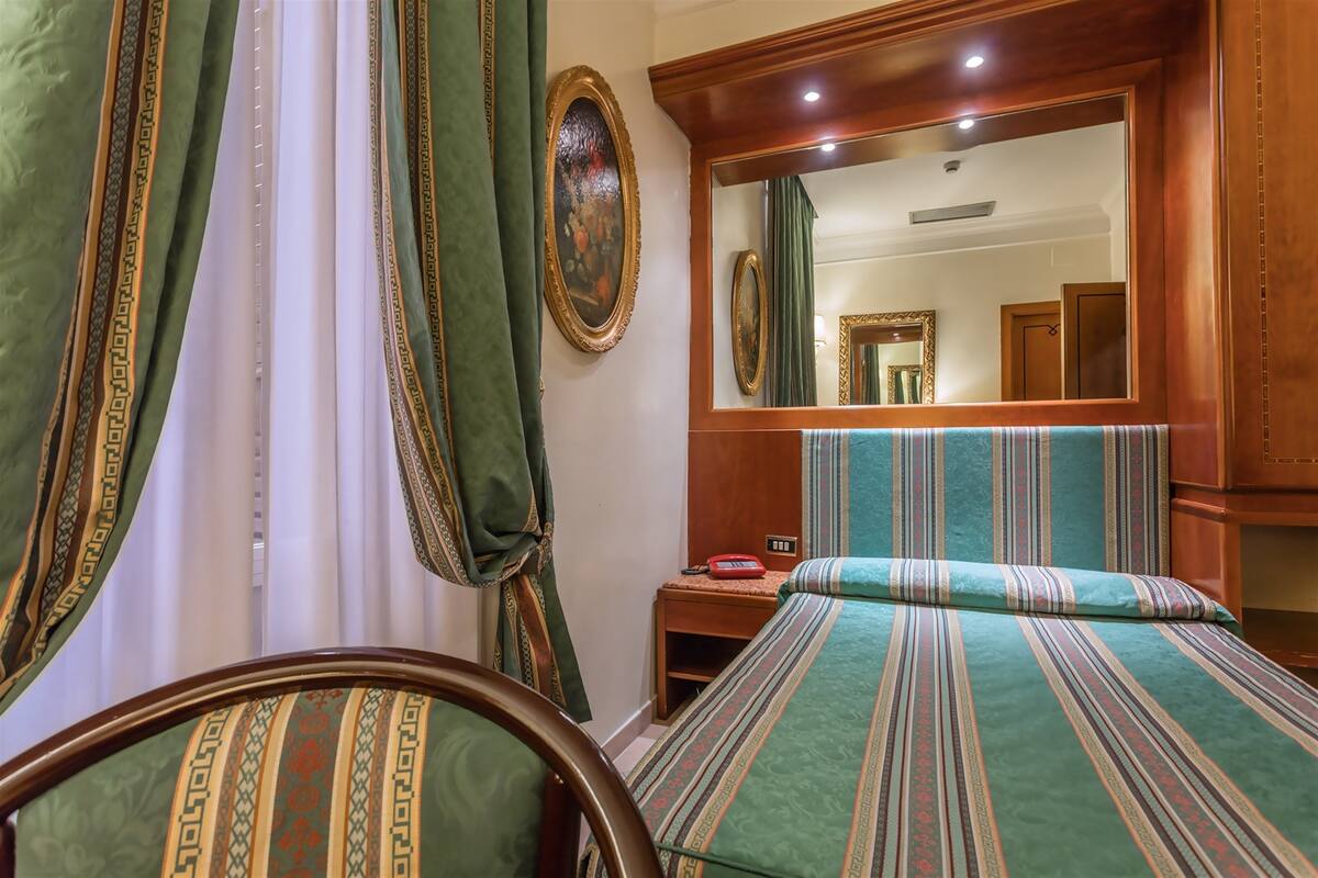 Une chambre d’hôtel avec un lit, une table de chevet, un miroir et des rideaux.