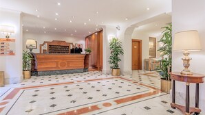 A hotel lobby with a reception desk, marble flooring, potted plants, and a seating area with a sofa. - Raeli Hotel Luce (Rome)