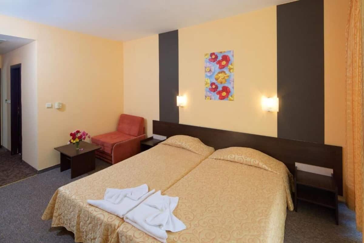 A hotel room with a double bed, a small table with a vase of flowers, a red chair, and a painting on the wall.