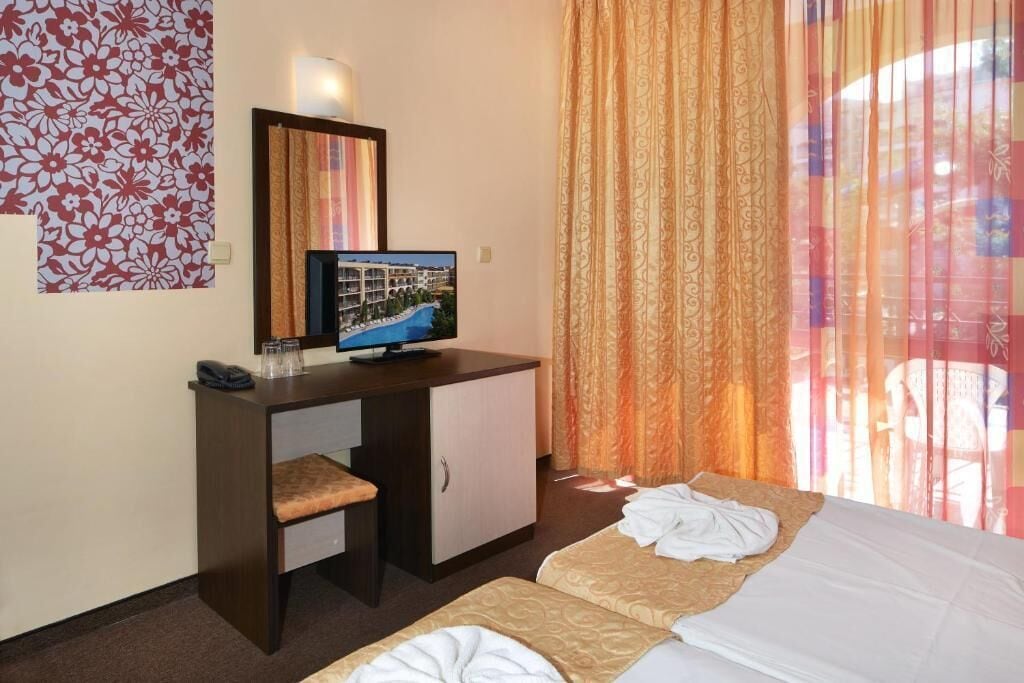 A hotel room with a desk, a television, two beds, and a window with curtains.