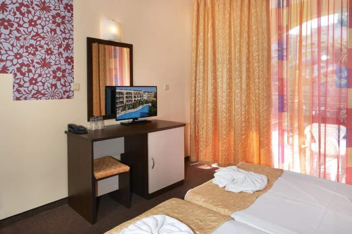 A hotel room with a desk, a television, two beds, and a window with curtains.