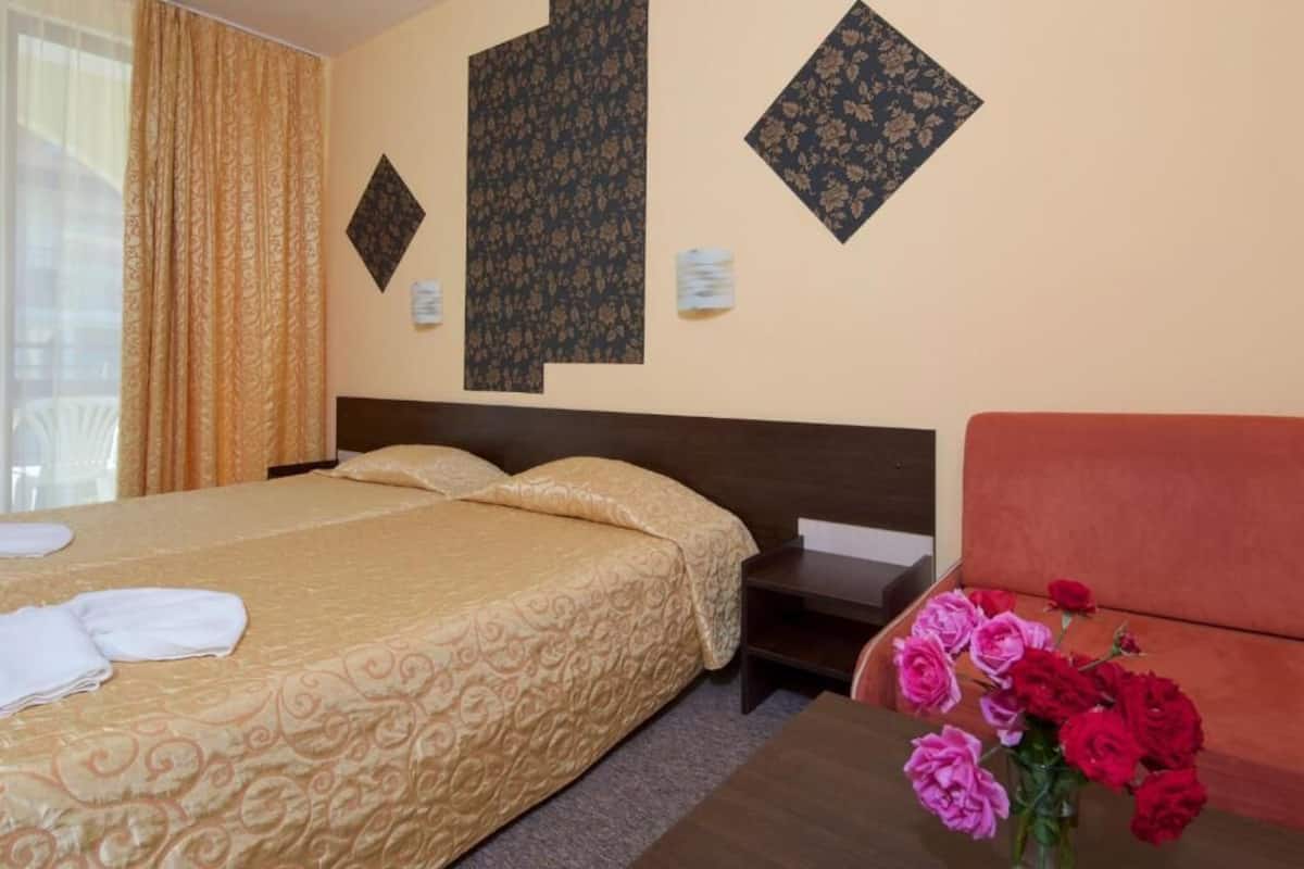 A hotel room with a bed, a sofa, a nightstand, and a vase of flowers.