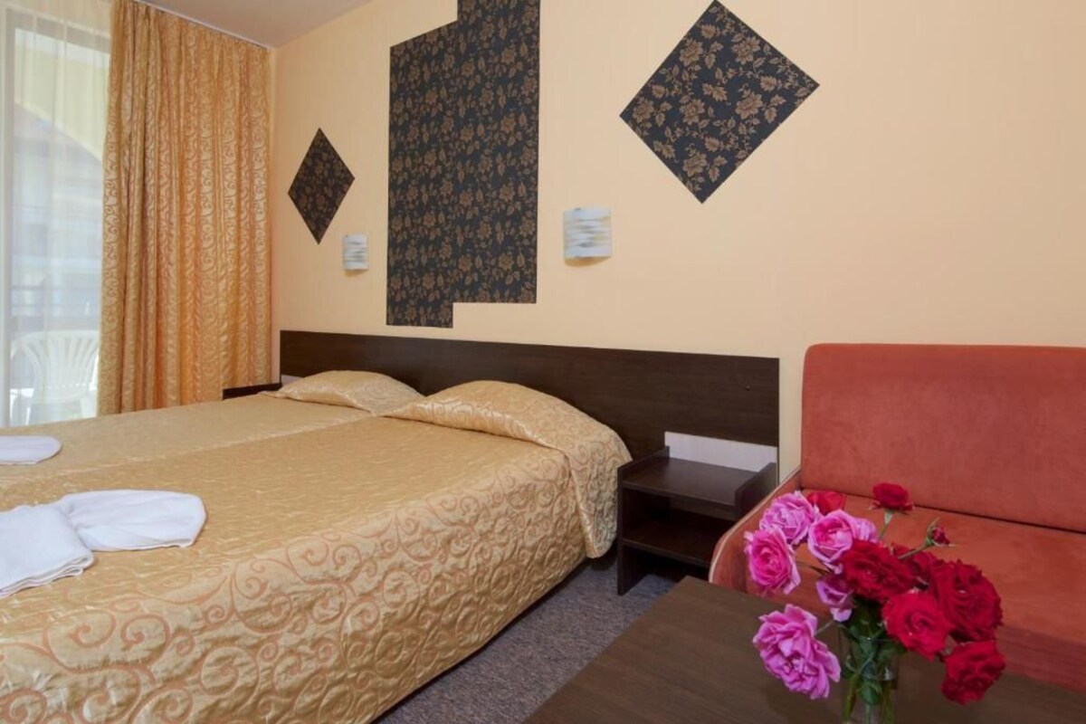 A hotel room with a bed, a sofa, a nightstand, and a vase of flowers.