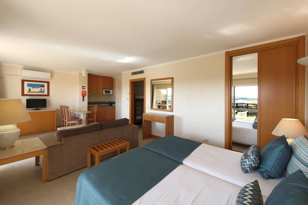 A hotel room with a bed, a sofa, a desk, a mirror, and a view of the outside.