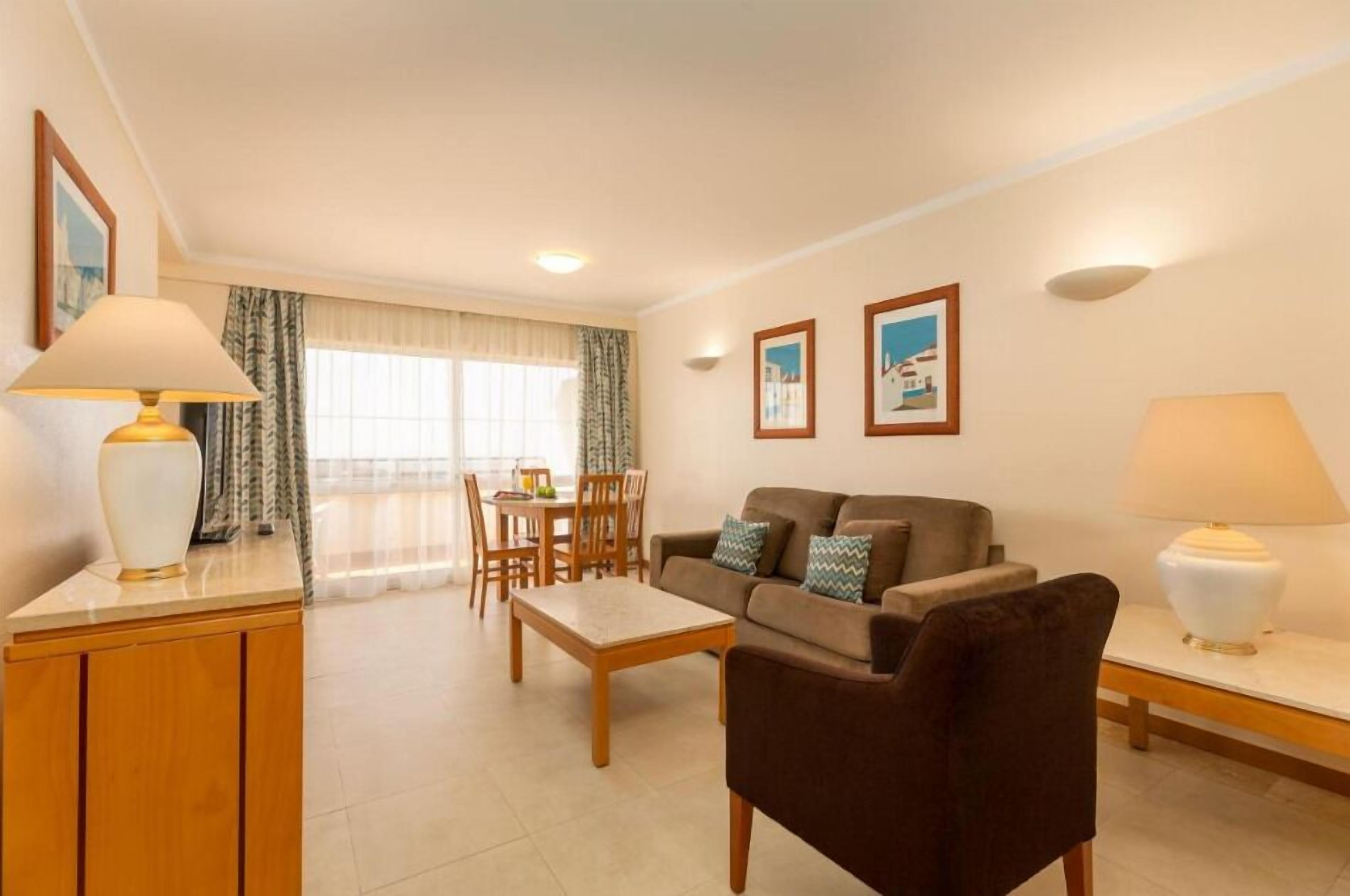 Een woonkamer met een bank, salontafel en lampen. Er is een eethoek met een tafel en stoelen.