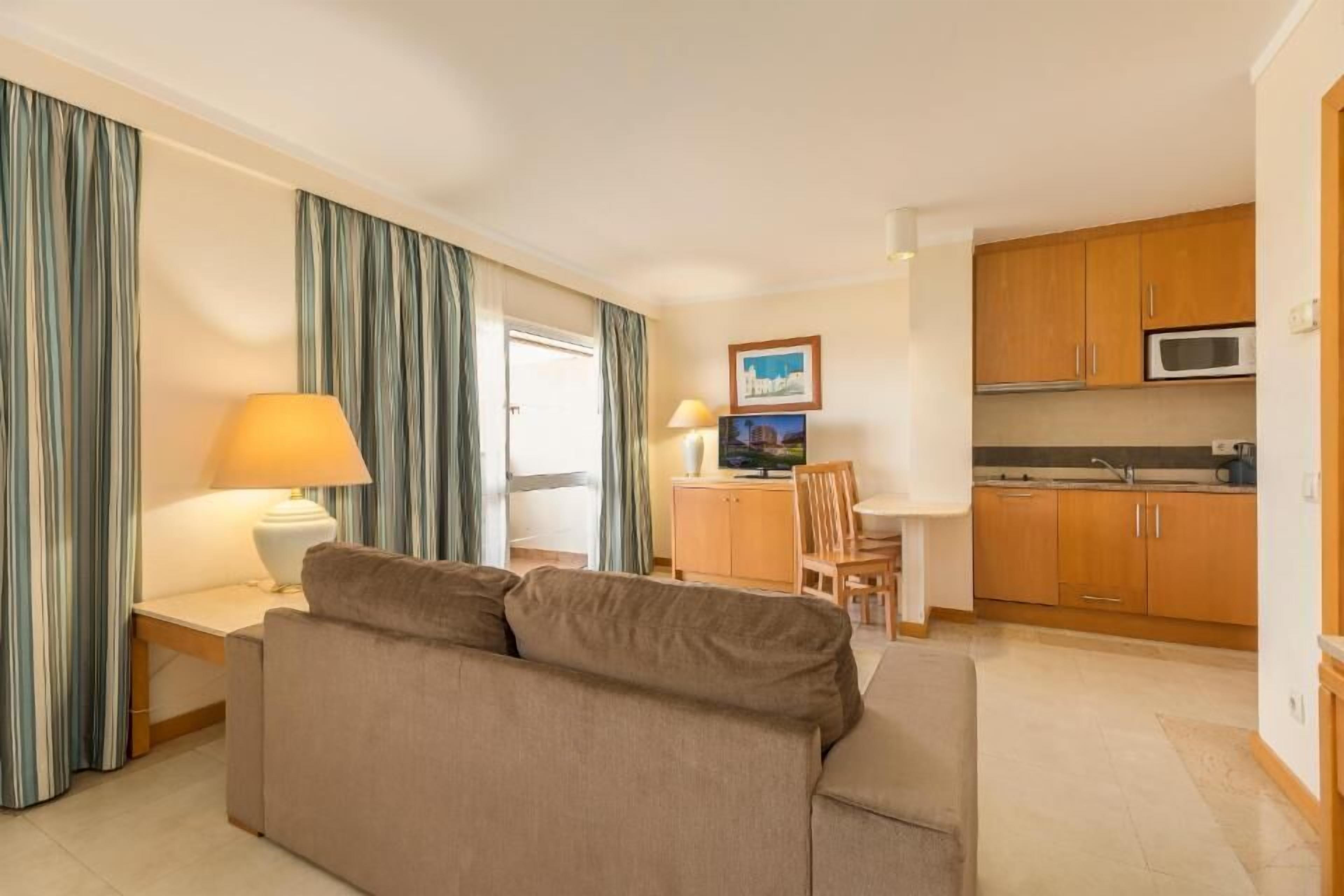 Un espacio habitable compacto con sofá, mesa de comedor, televisor y zona de cocina.