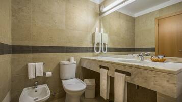 A bathroom with a sink, toilet, and bidet. There are towels hanging on the wall and a basket on the counter.