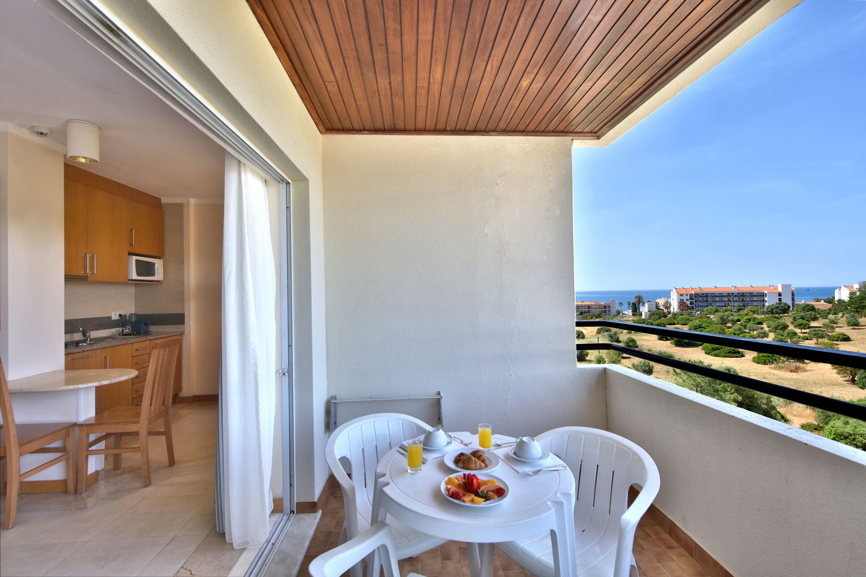 Un balcón con una mesa dispuesta para el desayuno, vistas a la playa y una zona de cocina.