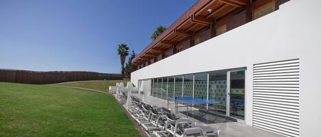 A modern building with a covered outdoor seating area, including lounge chairs and a ping pong table.