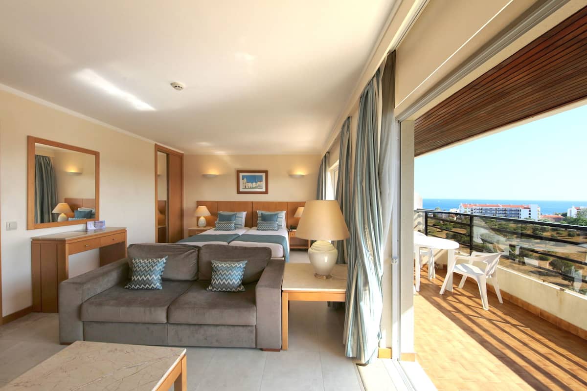 A modern hotel room with a balcony, a sofa, a bed, and a desk.