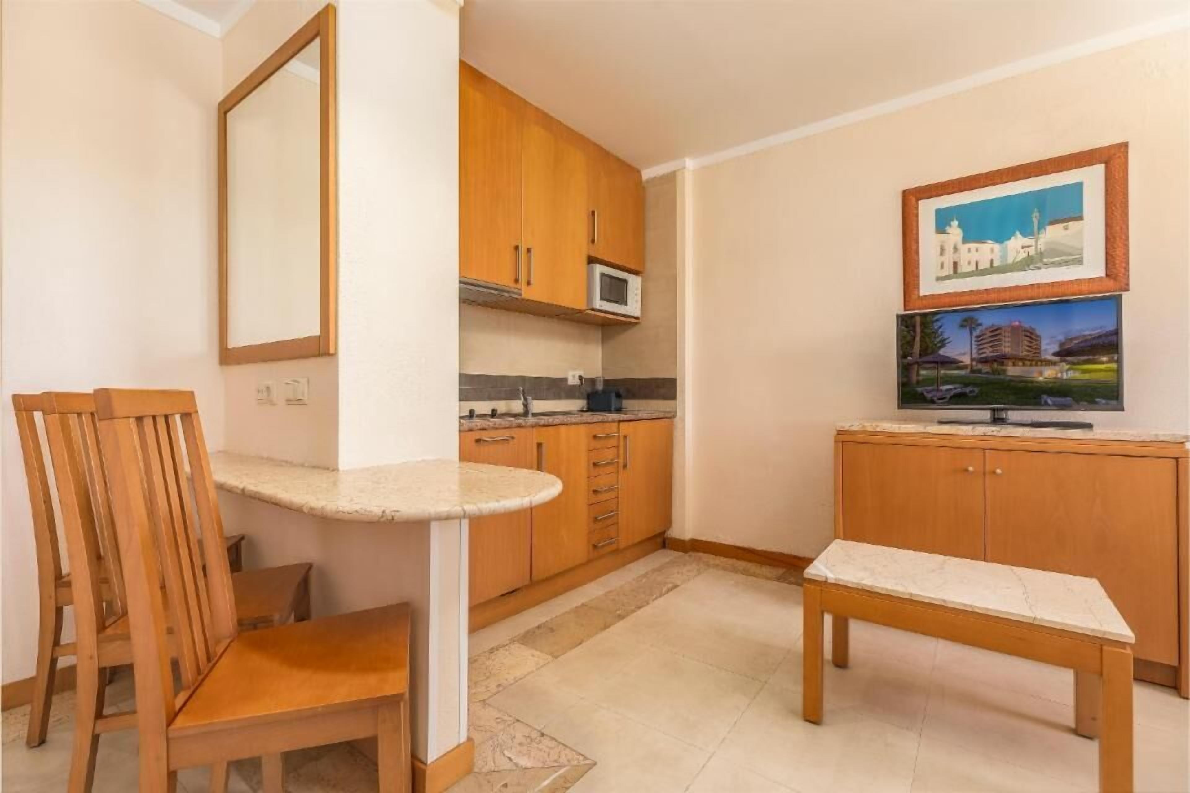 Una cocina pequeña con armarios de madera, un microondas, una mesa de comedor y un televisor.