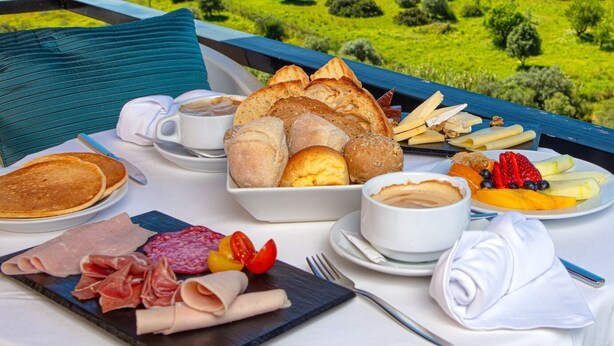 A breakfast table with pastries, fruits, and meats, overlooking a coastal landscape with greenery and buildings. - Interpass VAU Hotel & Apartaments (Portimão)