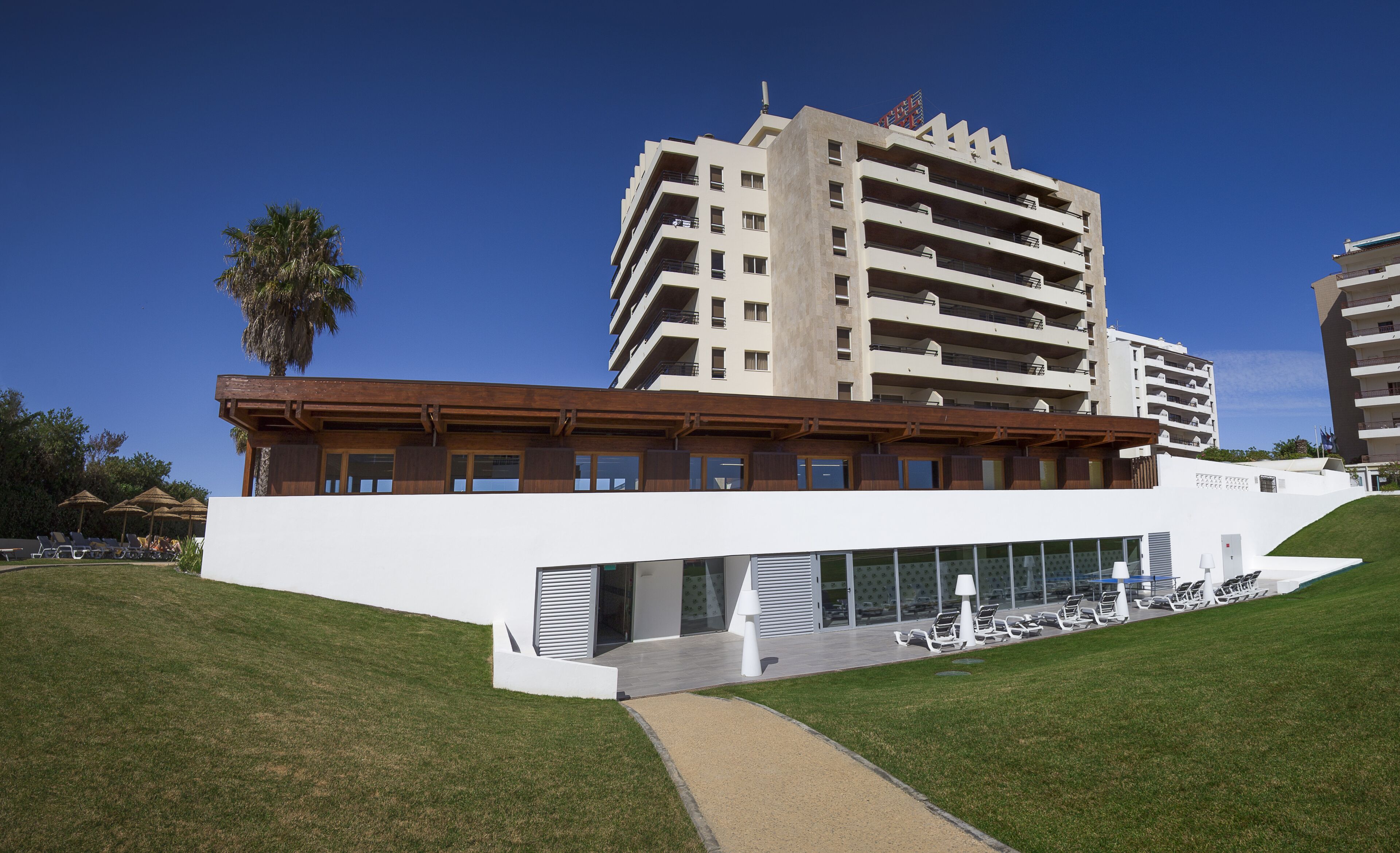 Un hôtel moderne doté d’un toit plat, de nombreux balcons et d’un espace piscine avec des chaises longues.
