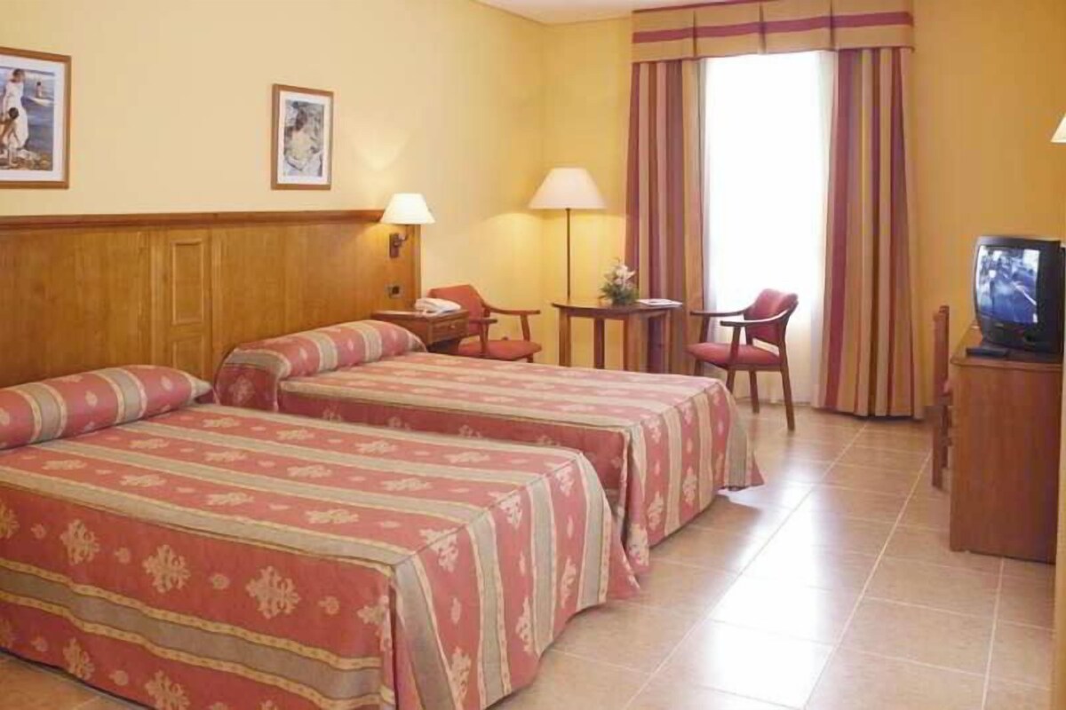 A hotel room with two beds, a television, a desk, and a chair.
