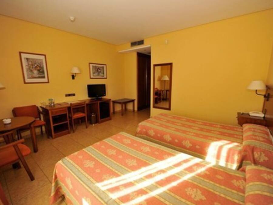 Habitación de hotel con dos camas, un escritorio, una silla, un televisor y dos lámparas.