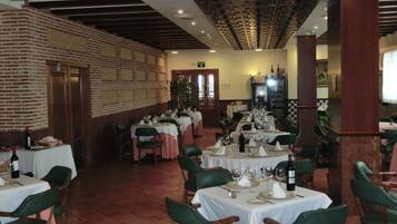 Un restaurant doté de nombreuses tables dressées pour le service, avec un mur en briques et un plafond en bois.