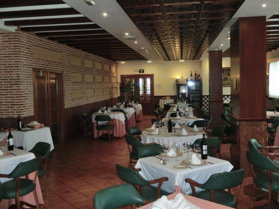 Un restaurant doté de nombreuses tables dressées pour le service, avec un mur en briques et un plafond en bois.