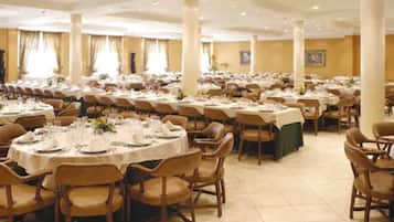 Een ruime balzaal met ronde tafels gedekt voor een diner, omringd door houten stoelen.