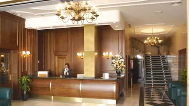 A hotel lobby with a reception desk, a chandelier, a staircase, and a checkered floor. - Hotel Lozano (Antequera)