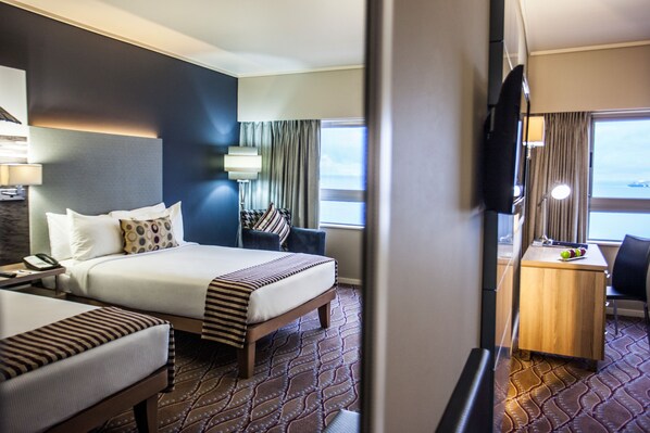A hotel room with a bed, bedside table, lamp, and a desk with a chair. - Garden Court Marine Parade (Durban)