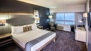 A hotel room with a large bed, a desk with a lamp, a chair, and a view of the sea. - Garden Court Marine Parade (Durban)