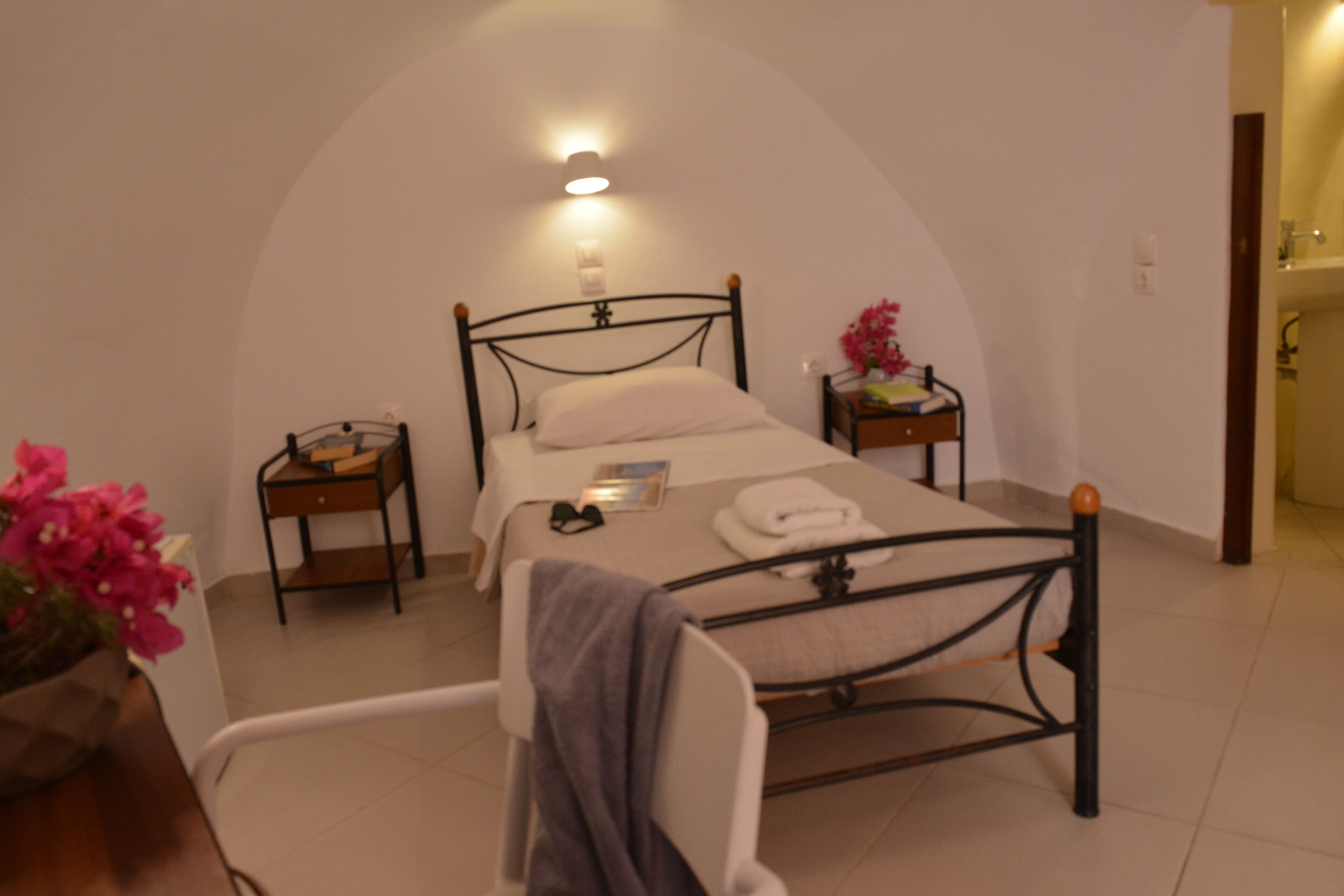 A bedroom with a single bed, a bedside table, a nightstand, a lamp, and a flower vase.