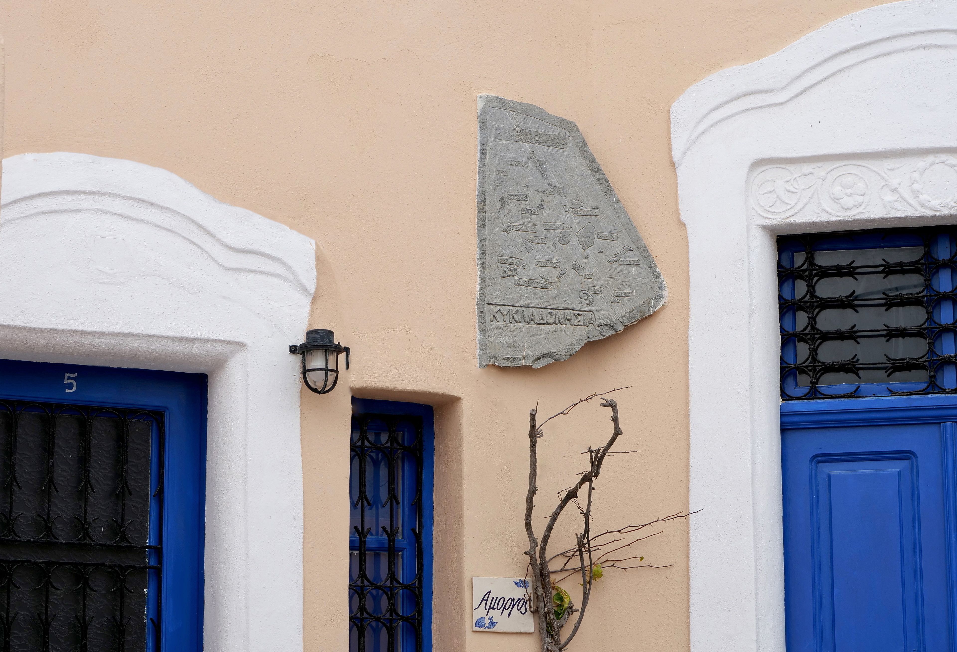 Facciata di un edificio con porte blu, una targa in pietra e un piccolo cartello.