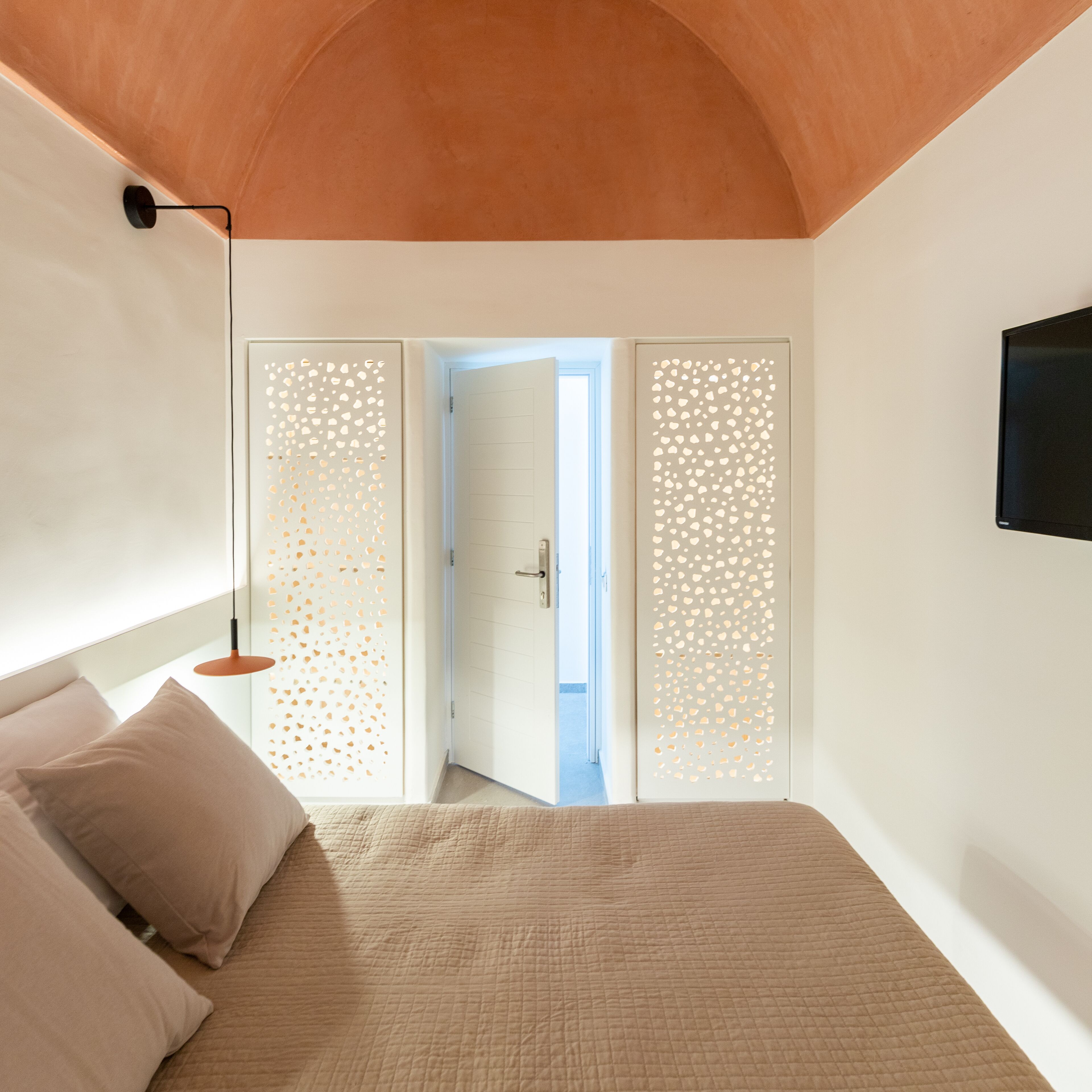 A bedroom with a bed, a nightstand, a wall-mounted TV, and a door leading to a balcony.