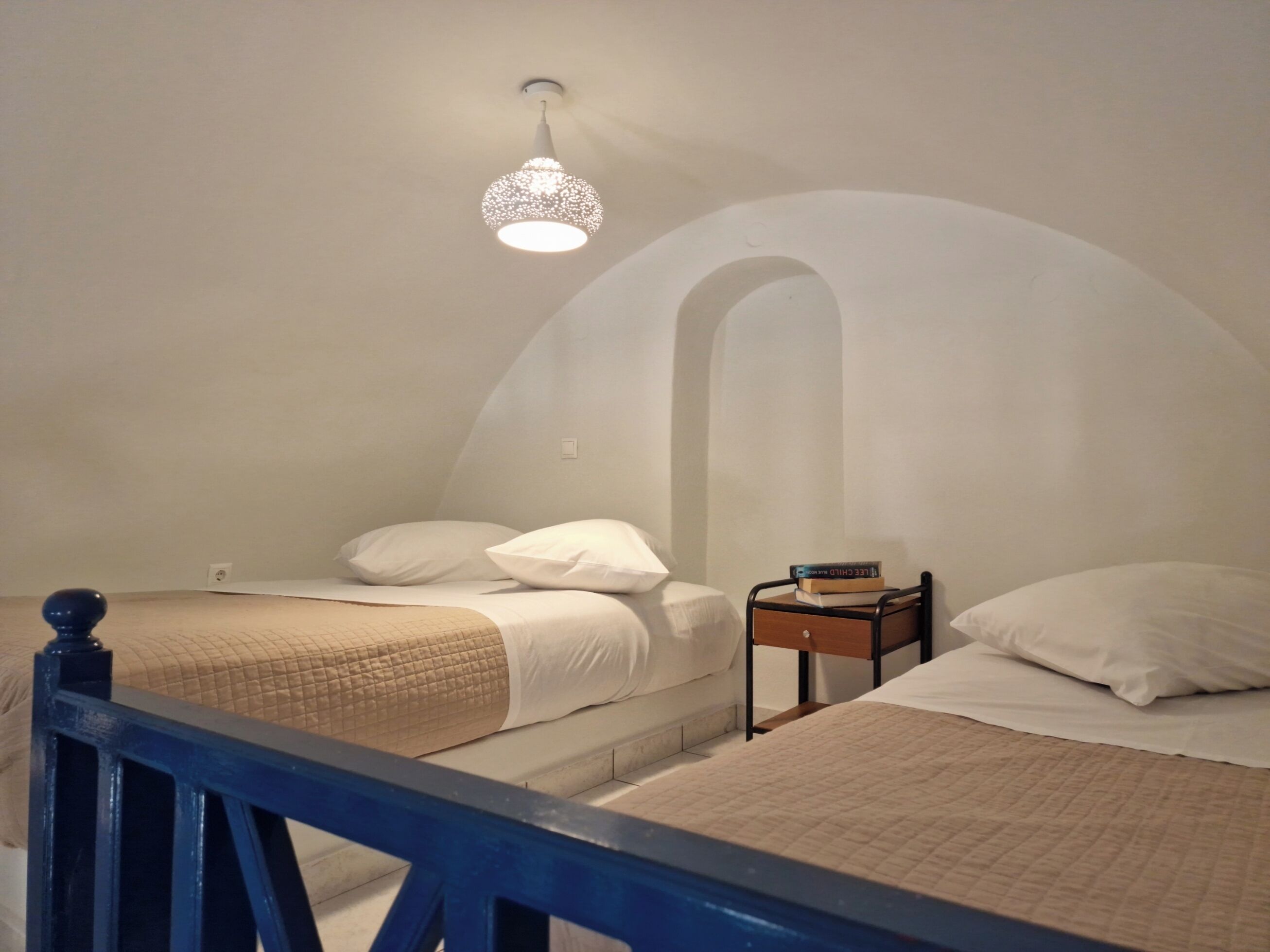 Un dormitorio con dos camas, una mesita de noche y una lámpara colgante.
